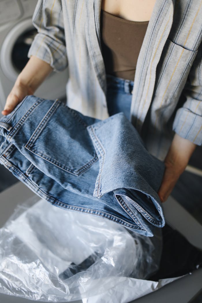 journey-01 Woman in striped shirt holding folded denim jeans in home laundry setting.