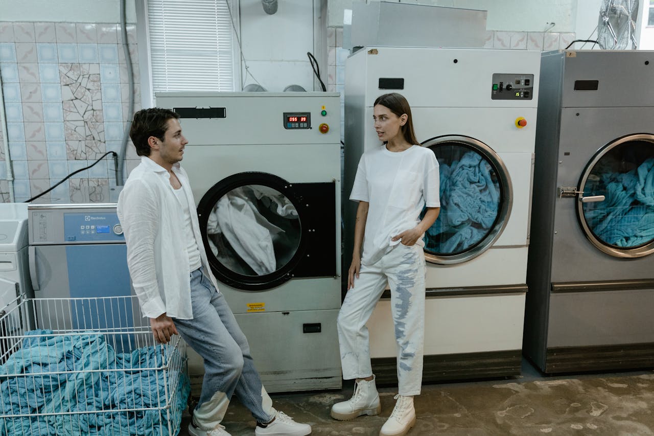 services-04 Two young adults have a conversation in a modern laundry facility, surrounded by washing machines.