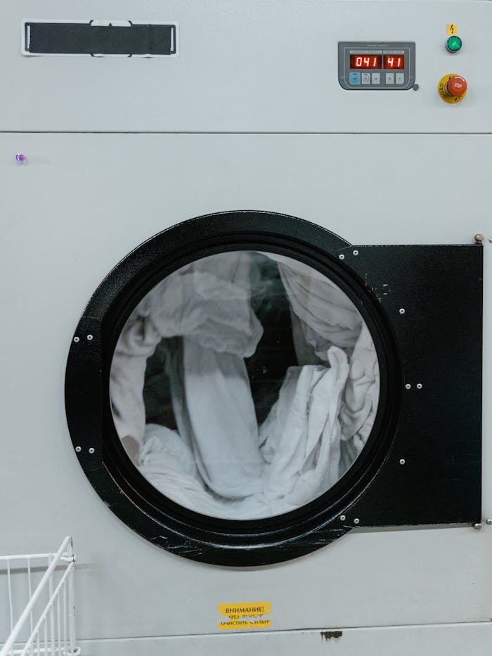 Close-up of a washing machine in a laundromat with clothes spinning inside.